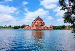 The orange sandstone historic tomb of Sher Shah Suri sits in the middle of a reflective body of blue water. 