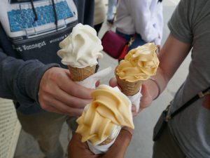 Three hands hold ice cream, swirled in cones. 