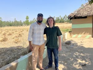The author standing next to Shamshaad Bhai in front of a Dero and a field of wheat in the Van Gujjar Basti.