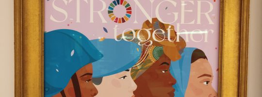 Gold Picture frame with four women from diverse countries, with the words Stronger Together across the top of the frame