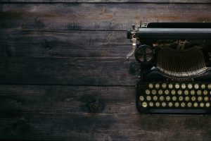 Image of black typewriter on wooden desk. Typewriter positioned on right side of image.