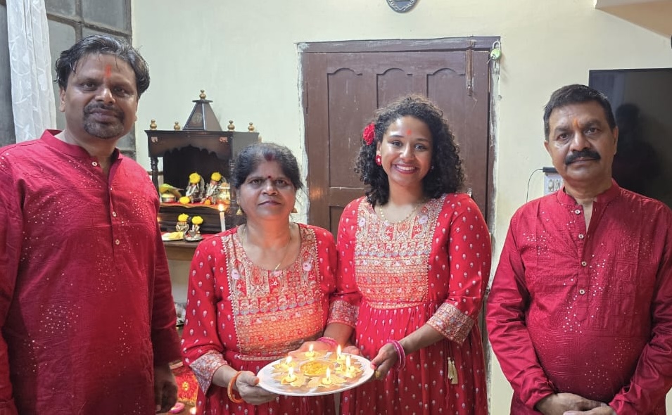 Courtney takes a photo with three other individuals during Diwali. All are dressed in red. Courtney and one woman are holding a tray of diyas.