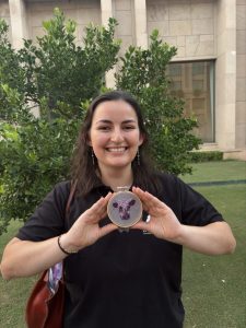 Erica holding a small embroidery hoop that is stitched with a cow in different shades of purple.