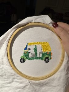  A picture of an embroidery hoop with a green and yellow rickshaw stitched by Erica. 