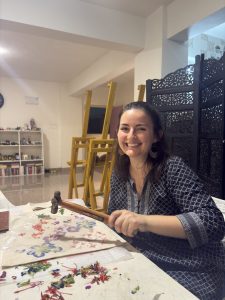 Erica holds a hammer as she decorates a tan canvas tote bag with the pigment of fresh flowers. 