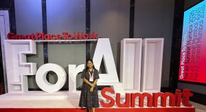 The author stands in front of a large “For All Summit” installation with “Great Place To Work” signage at the event venue.