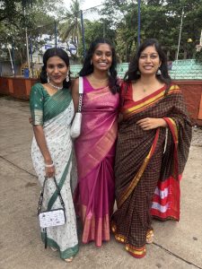 Sarina in a pink saree. On her left is a woman in a green and white saree, and on her right is a woman in a brown saree.